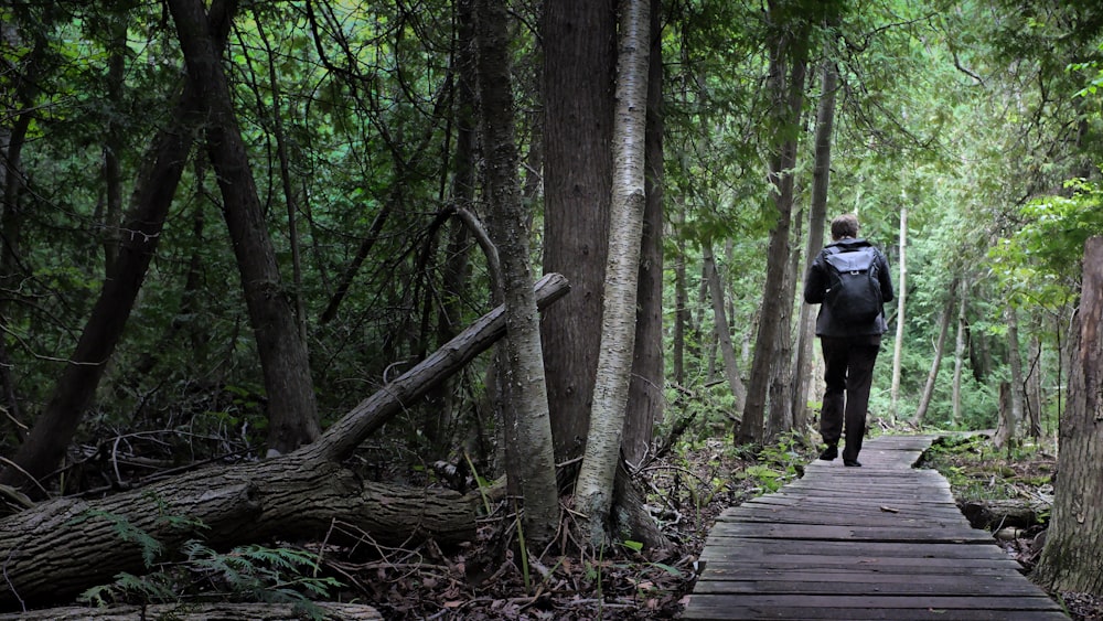 man in black jacket and black pants walking on wooden bridge