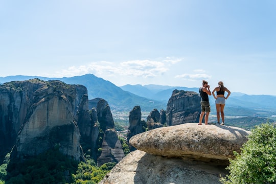 man and woman standing on rock formation during daytime in Meteora Greece