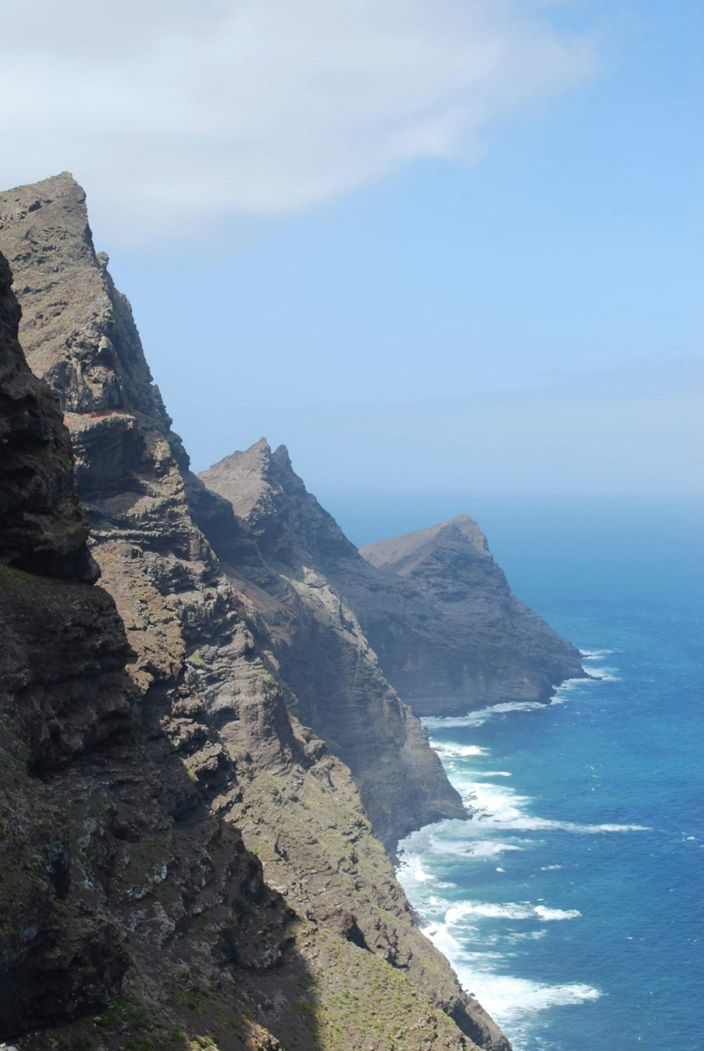 brown rocky mountain beside blue sea under blue sky during daytime