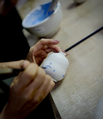 Someone painting a small vase with blue detailing