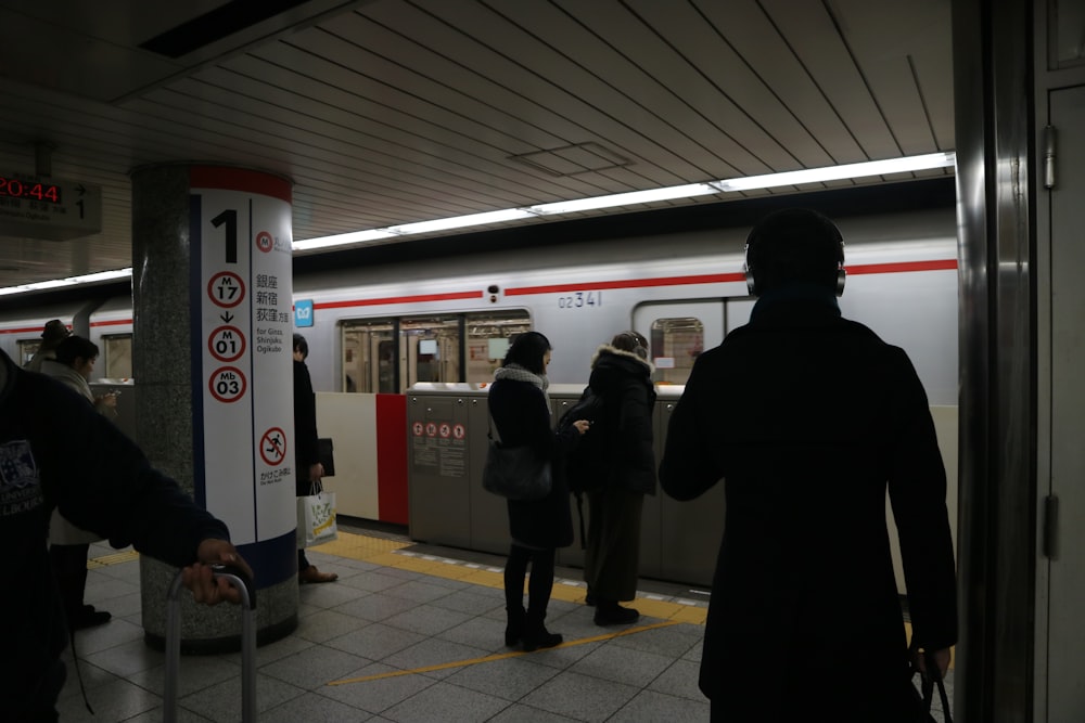 man in black coat standing near red train