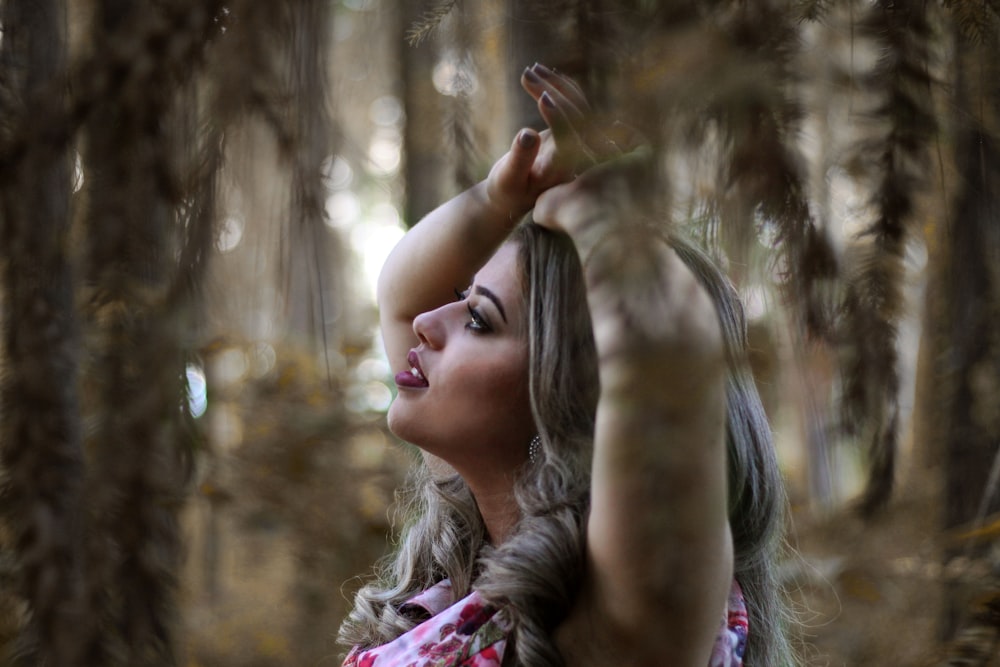 girl in pink and white floral shirt standing near brown trees during daytime