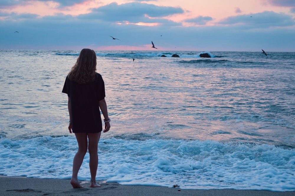 woman in black dress standing on seashore during sunset