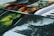 A collection of art prints displayed in layers, with vibrant colors and dynamic scenes. The foreground features a fantasy landscape in green hues with a silhouette of a creature. Other sections display fiery imagery and detailed character designs.