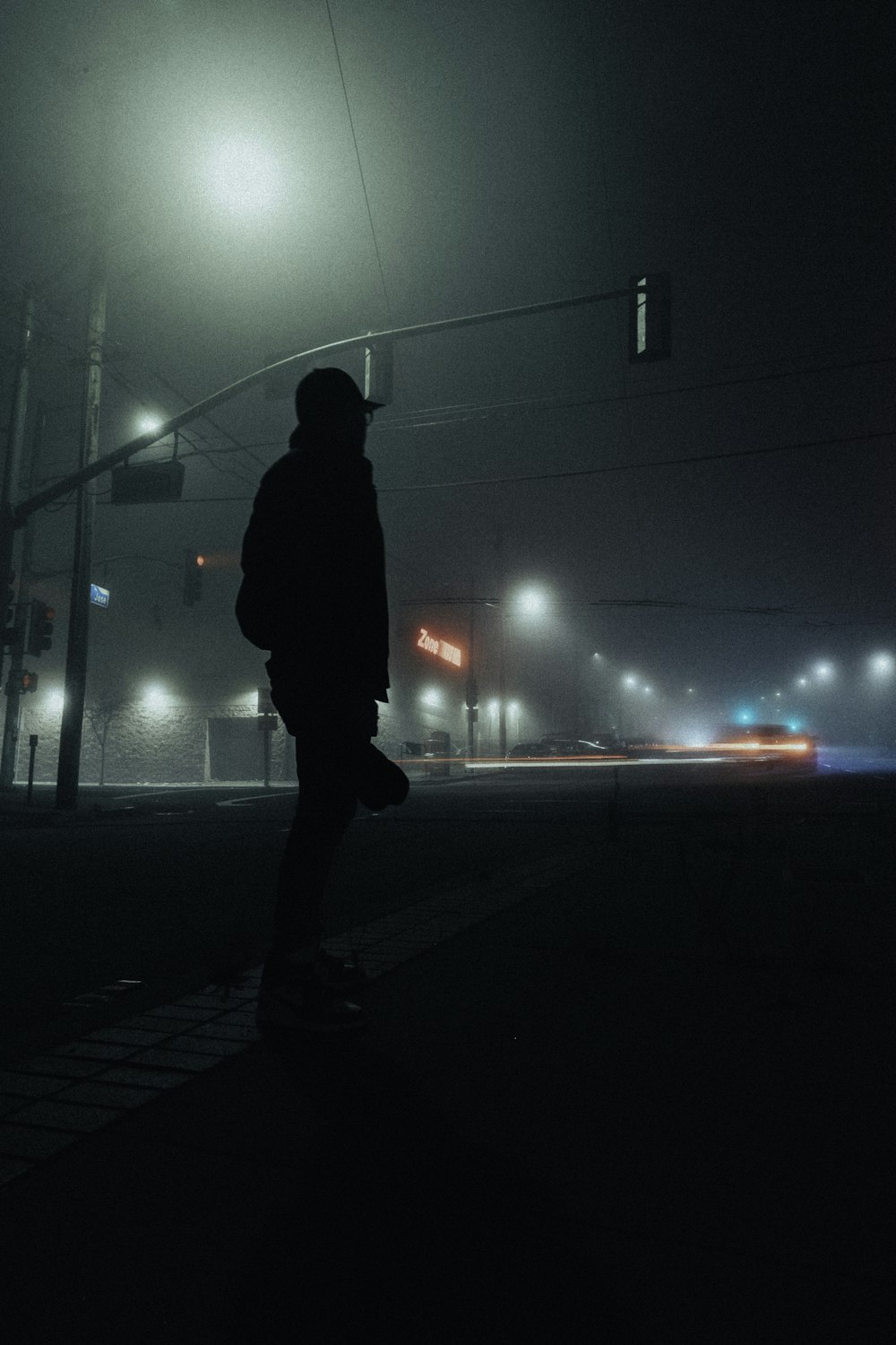 man in black hoodie standing on sidewalk during night time