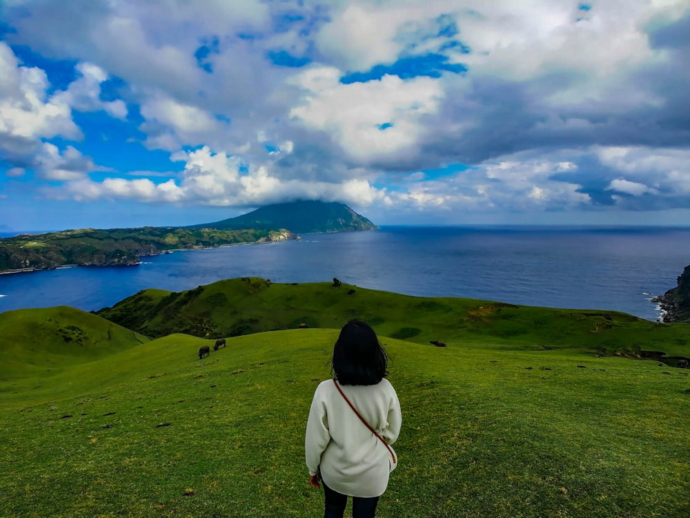 person in white hoodie standing on green grass field near body of water during daytime