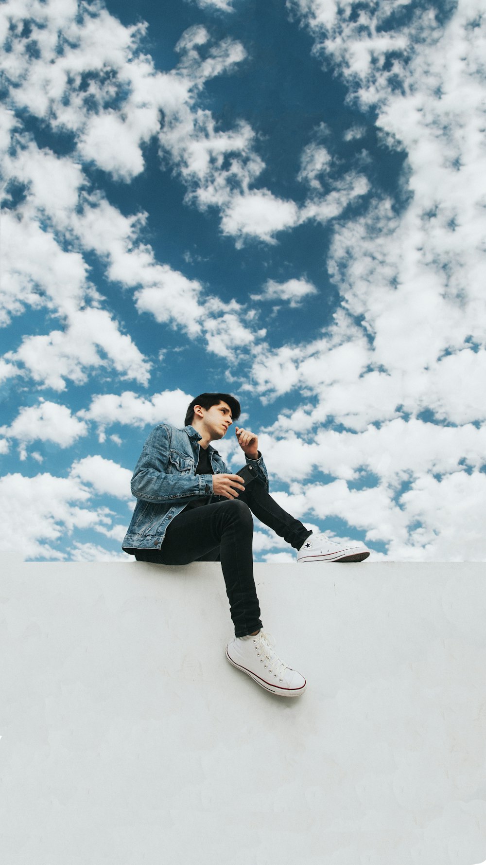 woman in blue denim jacket and black pants sitting on snow covered ground under white clouds