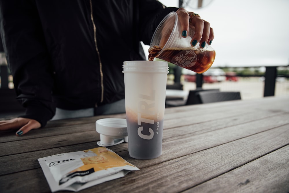 person holding clear plastic cup with brown liquid