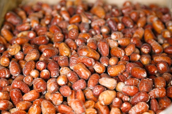 A close-up view of a large pile of red and brown dates, showcasing their glossy texture and slight variations in size and shape.