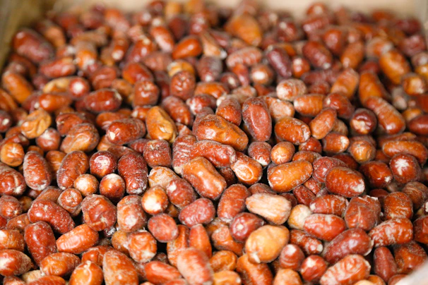 A close-up view of a large pile of red and brown dates, showcasing their glossy texture and slight variations in size and shape.