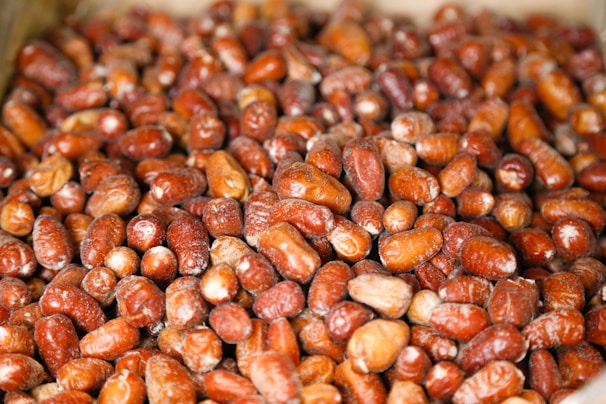 A close-up view of a large pile of red and brown dates, showcasing their glossy texture and slight variations in size and shape.
