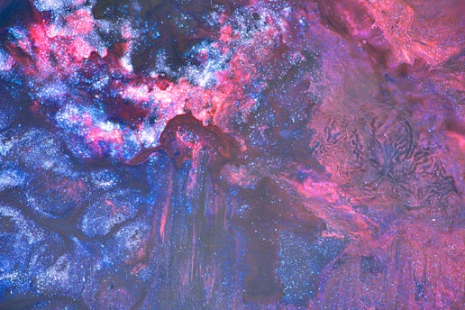Swirling patterns of vibrant blue, pink, and purple blend together with glittering textures, reminiscent of an abstract cosmos or nebula.