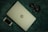 A closed HP laptop is placed on a textured green surface, alongside a black smartphone and a pair of headphones. The elements are arranged with the laptop centrally positioned, the phone to the bottom left, and the headphones to the top right. The color contrast between the light silver laptop and the dark accessories creates a balanced composition.