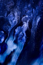 A mesmerizing abstract pattern featuring swirls of deep blue and black with bright white specks resembling stardust or galaxies. The fluid dynamics create a sense of depth and motion, evoking the vastness of space and the mystery of the cosmos.