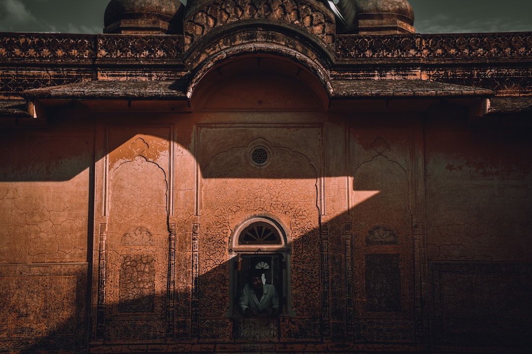 man in black jacket standing in front of brown concrete building, Glancing through history
