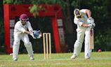 man in white and red jersey shirt and white pants holding brown wooden stick