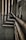 Multiple interconnected pipes run vertically and horizontally along the corner of a slightly worn and grimy wall. The pipes have a weathered and rusty appearance, suggesting they have been in place for some time. Some cables are also visible next to the pipes.