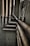 Multiple interconnected pipes run vertically and horizontally along the corner of a slightly worn and grimy wall. The pipes have a weathered and rusty appearance, suggesting they have been in place for some time. Some cables are also visible next to the pipes.