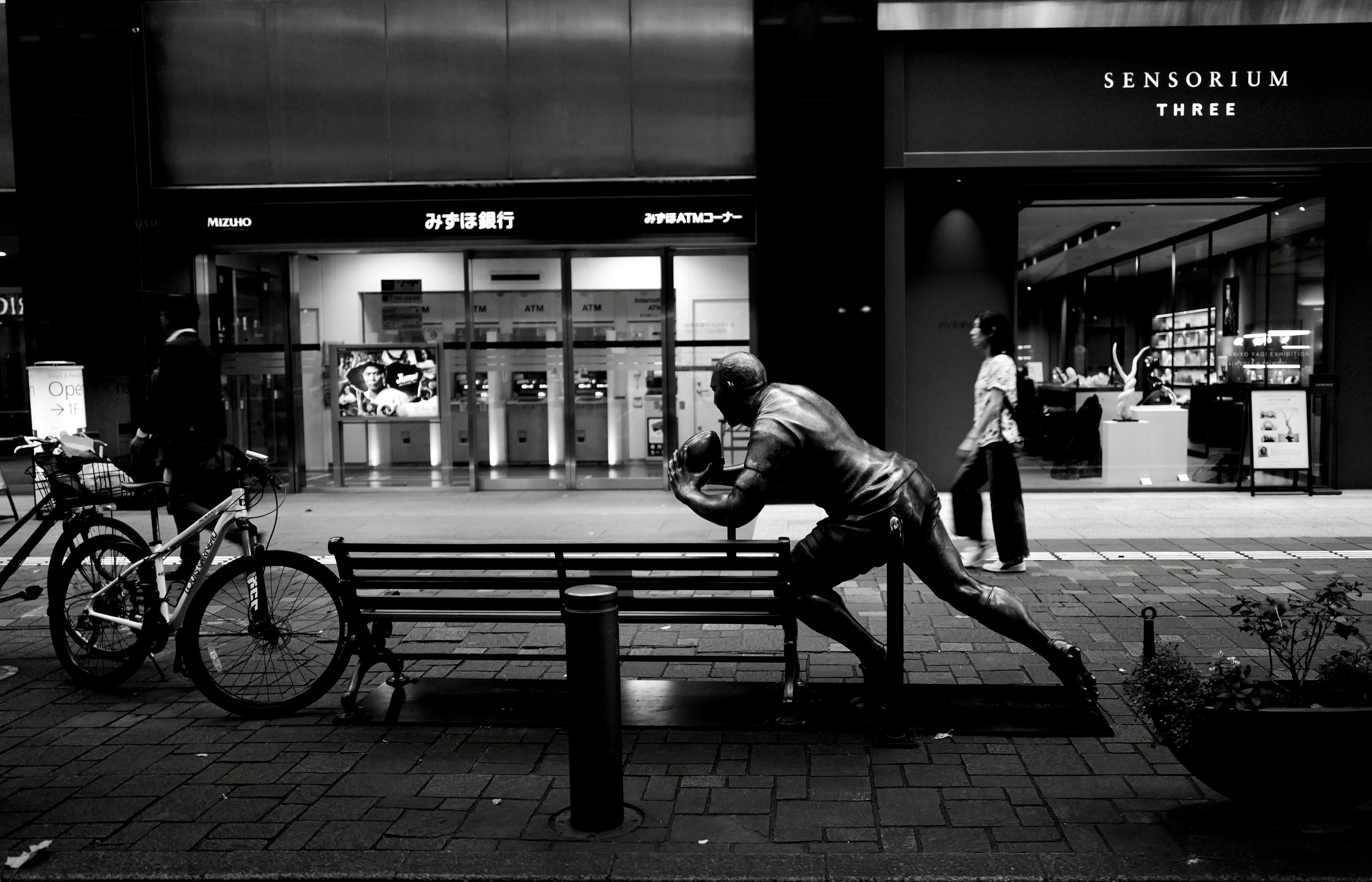 grayscale photo of man sitting on bench near building