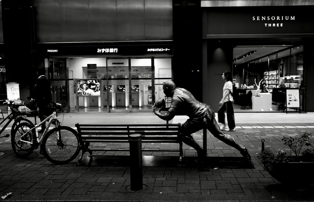 grayscale photo of man sitting on bench near building