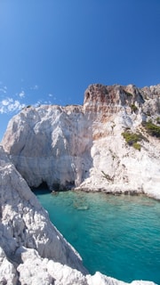 white rocky mountain beside blue sea under blue sky during daytime
