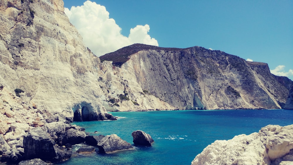 brown rocky mountain beside blue sea under blue sky during daytime