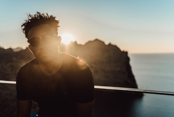 A person wearing classic aviator sunglasses standing by the beach during golden hour