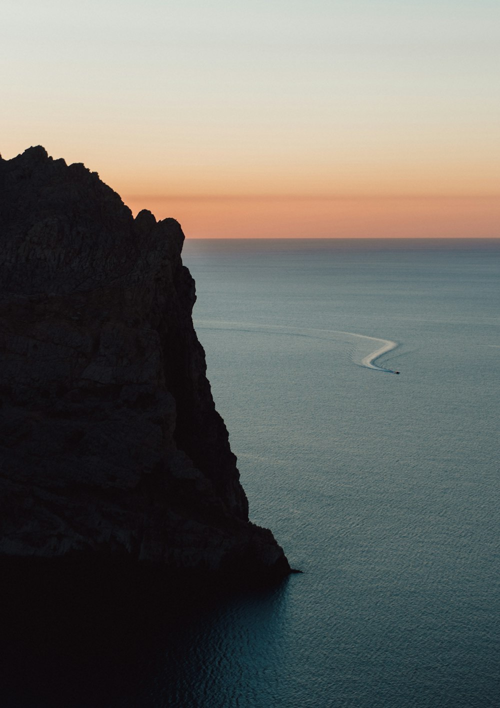 white sailboat on sea near brown rock formation during daytime