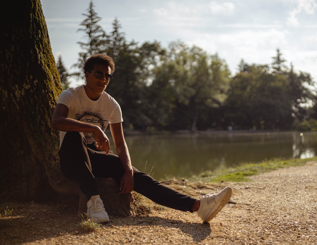 man in white crew neck t-shirt and black pants sitting on brown rock near body