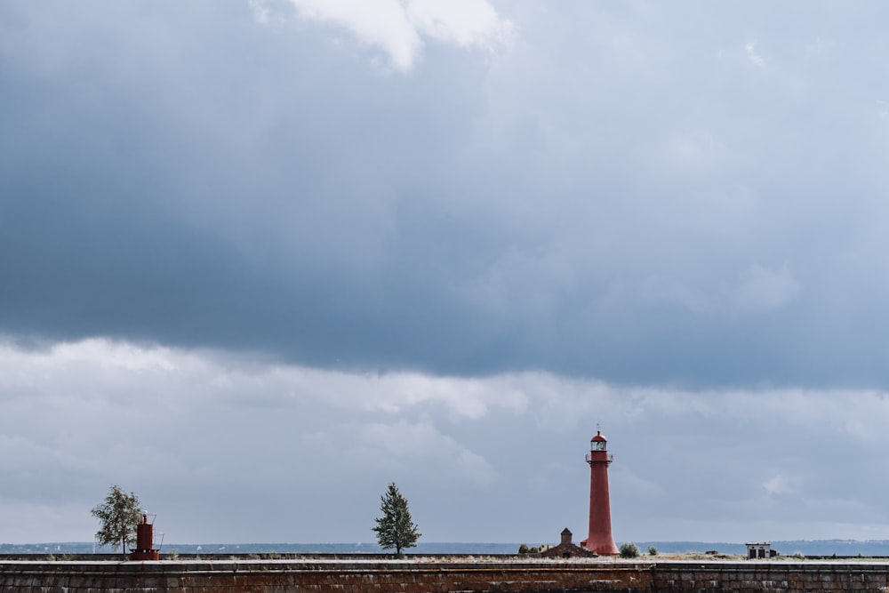 red and white lighthouse near green trees under white clouds and blue sky during daytime