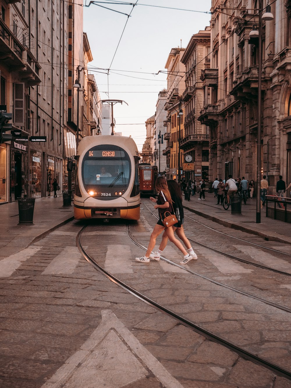 woman in black shirt walking on sidewalk near white and brown train during daytime