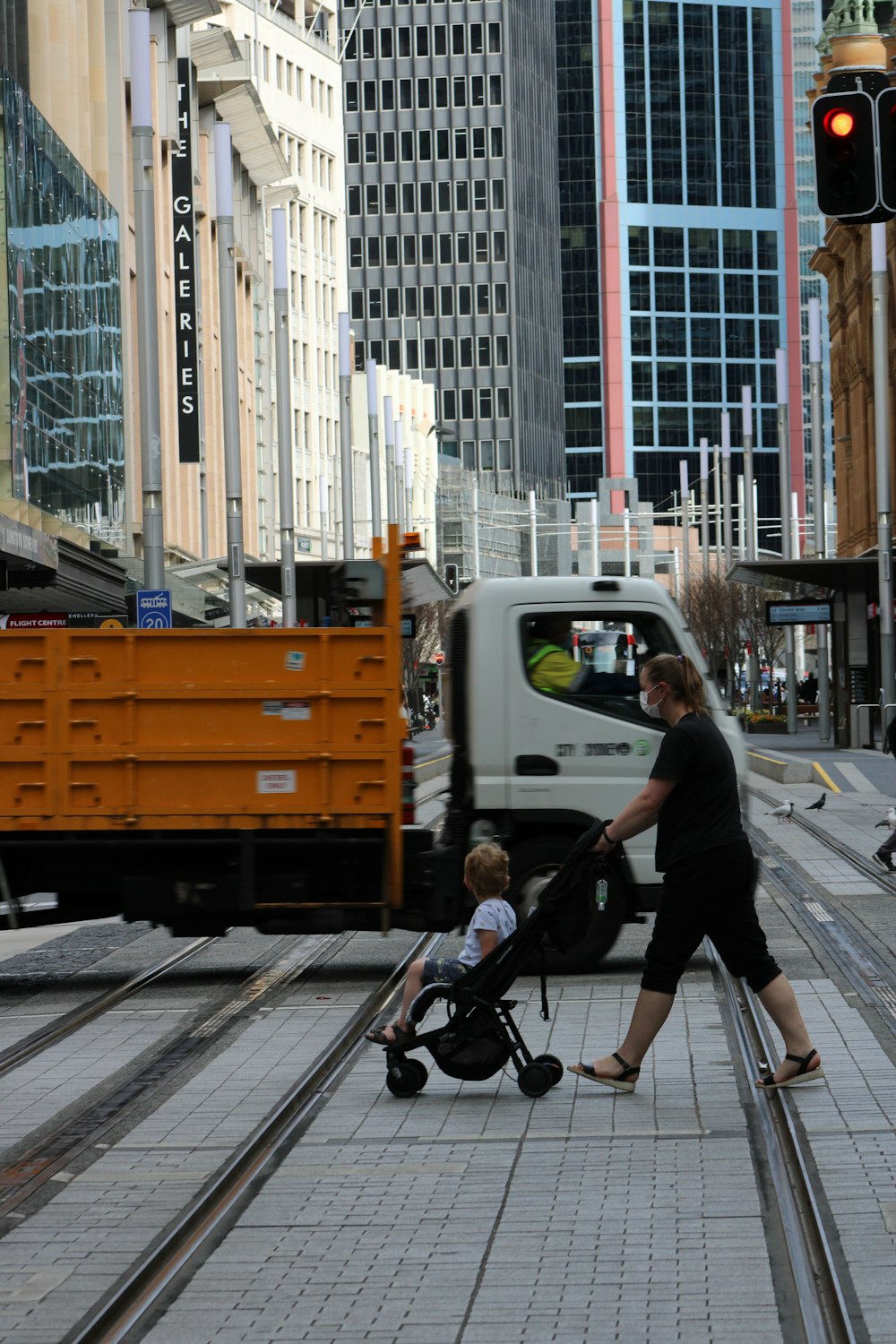 homme en chemise noire et pantalon noir marchant sur le trottoir avec une poussette noire pendant la journée