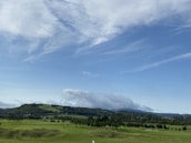 A scenic shot of a nine-hole golf course nestled among rolling green hills under a soft morning sky.