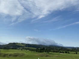 A scenic shot of a nine-hole golf course nestled among rolling green hills under a soft morning sky.