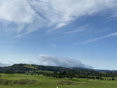 A wide shot of a minimalist golf course with rolling hills under a cloudy sky.