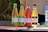 Four bottles of Wild Leaf Kombucha are lined up on a dark surface. Each bottle has a different flavor and label color: lime cucumber mint, apple ginger, raspberry lavender hibiscus, and vanilla chai. The background appears to be a natural, outdoor setting.