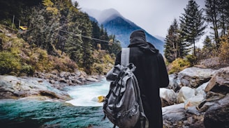 person in black hoodie standing near river in Kasol