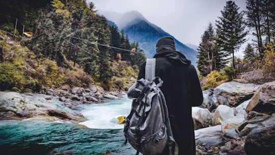 person in black hoodie standing near river during daytime in Kasol India