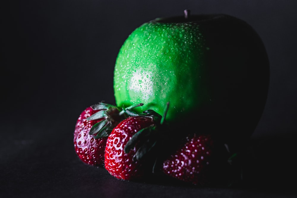 green apple with strawberries on black surface