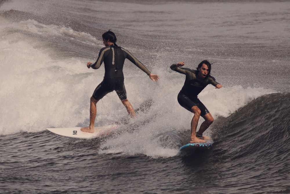 2 women in black wet suit surfing on sea waves during daytime