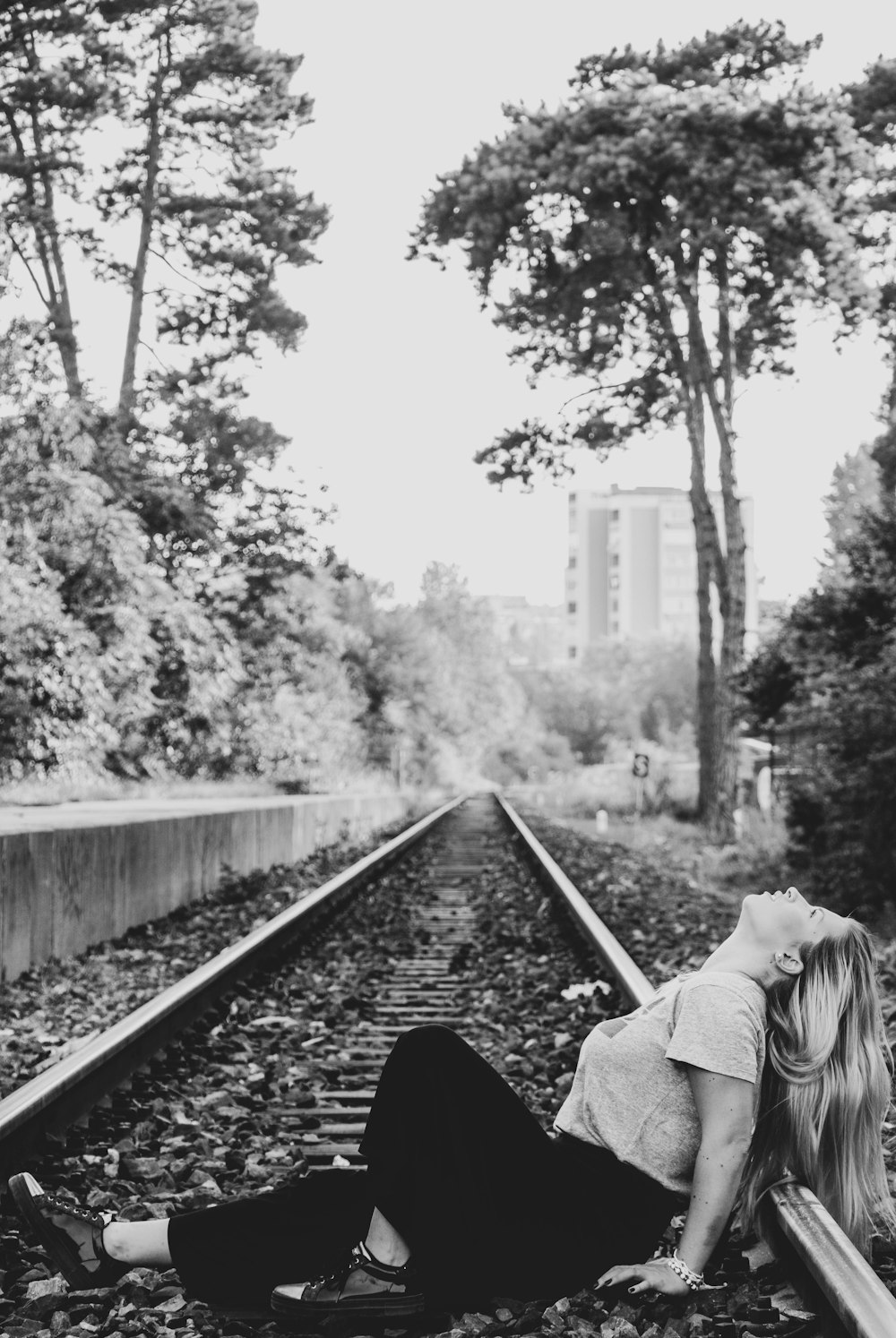 grayscale photo of woman sitting on train rail