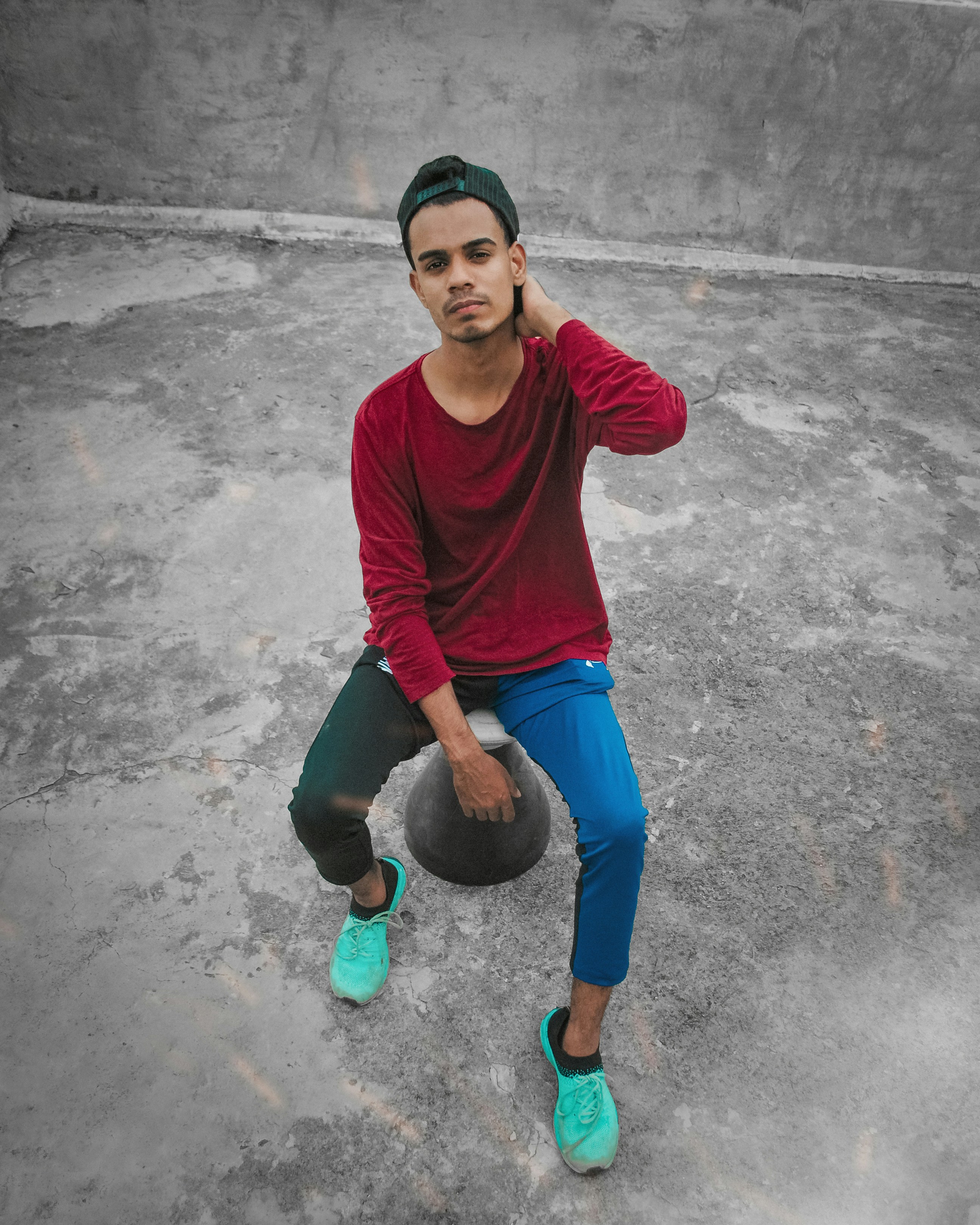Pria dengan kemeja lengan panjang leher kru merah dan jeans denim biru duduk di atas beton abu-abu
