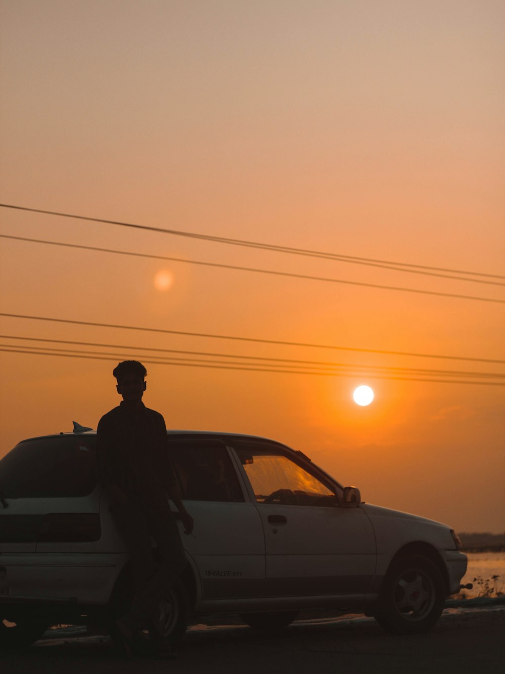 silhouette of man standing beside car during sunset