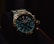 A luxury wristwatch with a metallic strap and a detailed, dark blue dial featuring multiple small dials and a prominently displayed brand name. The watch has a rugged yet elegant design with a polished metal case and intricate details on the crown and bezel.