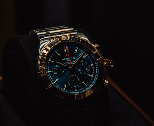 A luxury wristwatch with a metallic strap and a detailed, dark blue dial featuring multiple small dials and a prominently displayed brand name. The watch has a rugged yet elegant design with a polished metal case and intricate details on the crown and bezel.