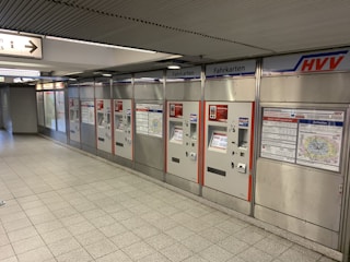 A row of ticket vending machines with the label 'Fahrkarten' in a subway station environment. The area is clean and well-lit, with metal paneling and informational maps and signage visible on the machines.