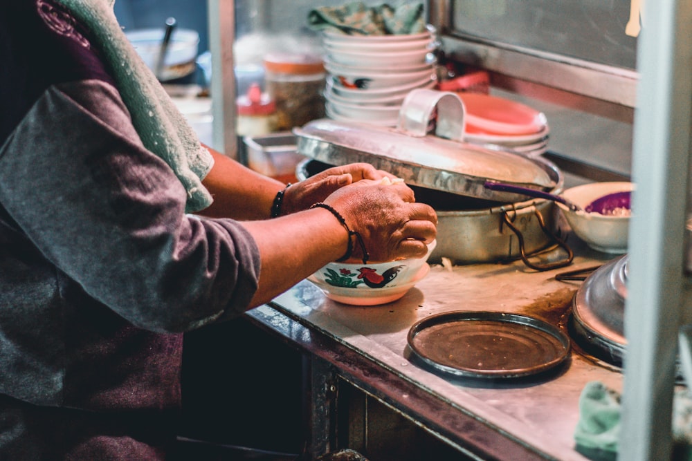 person in gray long sleeve shirt holding white ceramic bowl