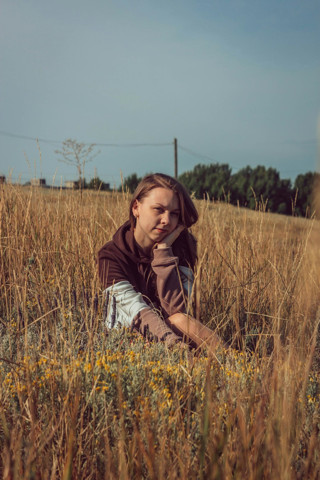 woman in brown jacket sitting on brown grass field during daytime