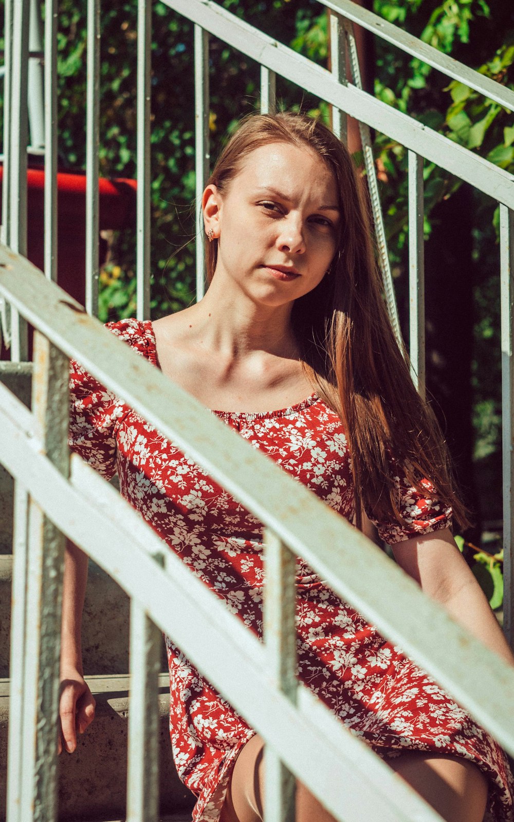 woman in red and white floral dress standing beside white wooden fence