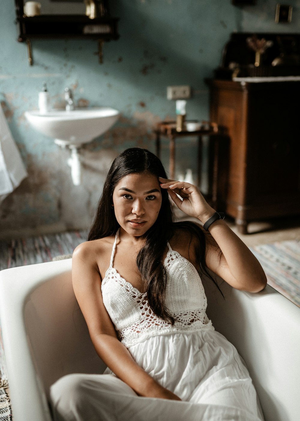 Frau in weißem ärmellosem Kleid sitzt auf weißer Keramikbadewanne
